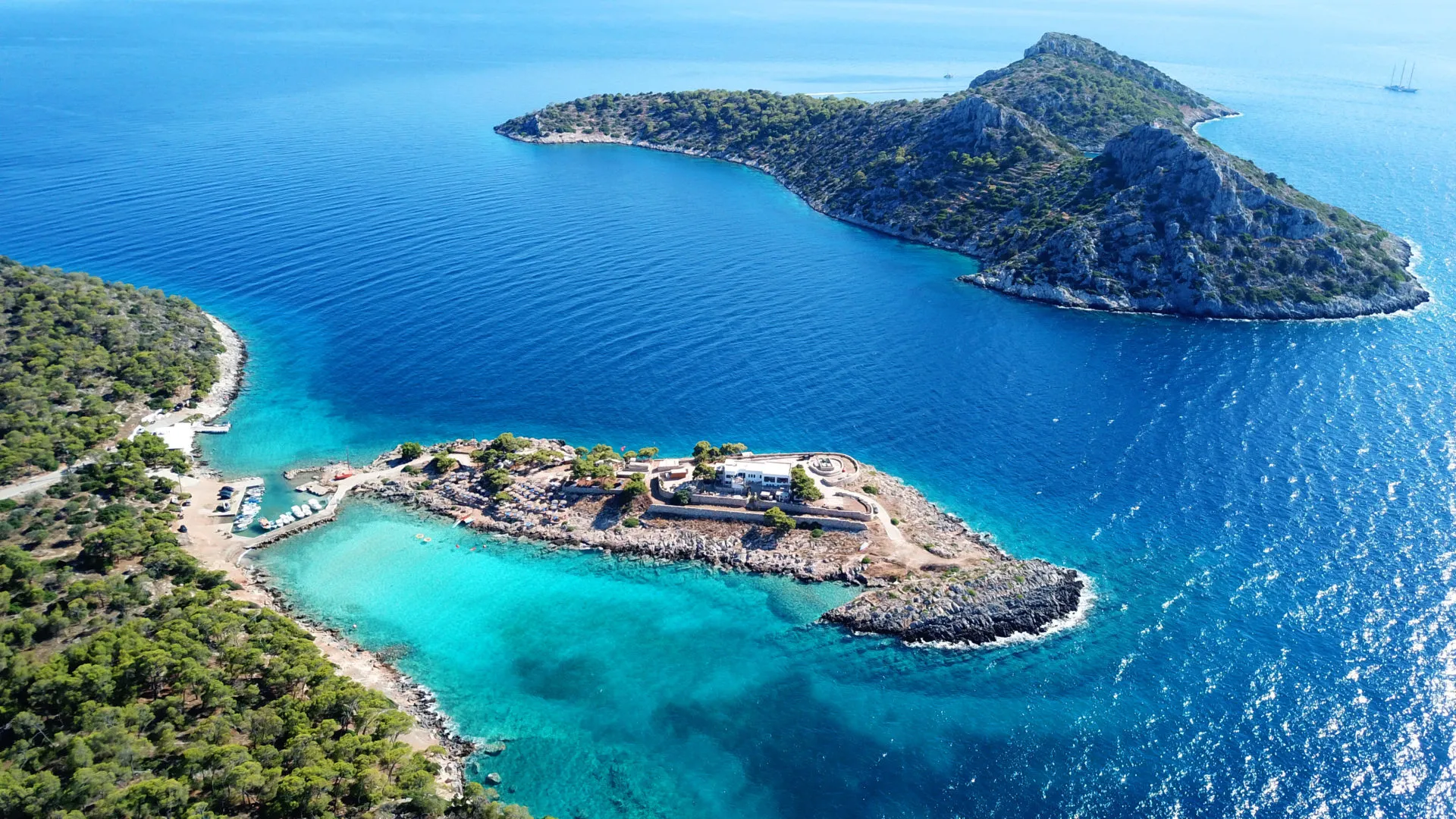 Aerial view of Aponisos Beach on Agistri Island, Greece, featuring turquoise water, pine trees, and small islets.
