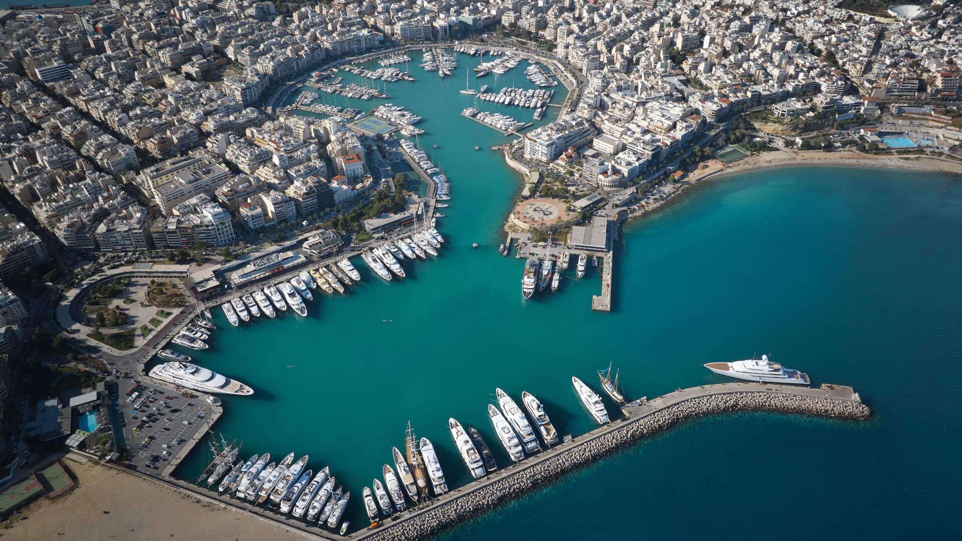 Aerial view of Zea Marina in Piraeus, Greece, with superyachts docked in the harbor and the city surrounding the marina.

