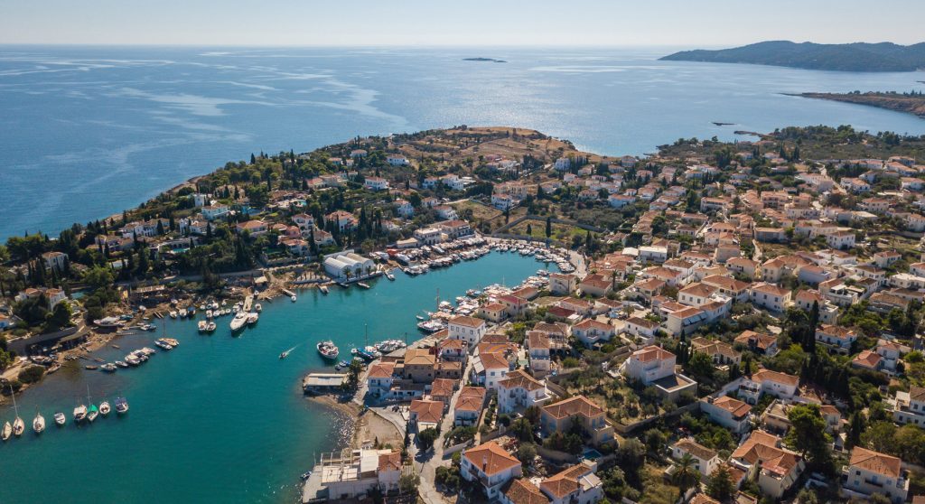 Aerial view of Spetses Island&rsquo;s old harbor with yachts docked and traditional houses stretching across the hillside.