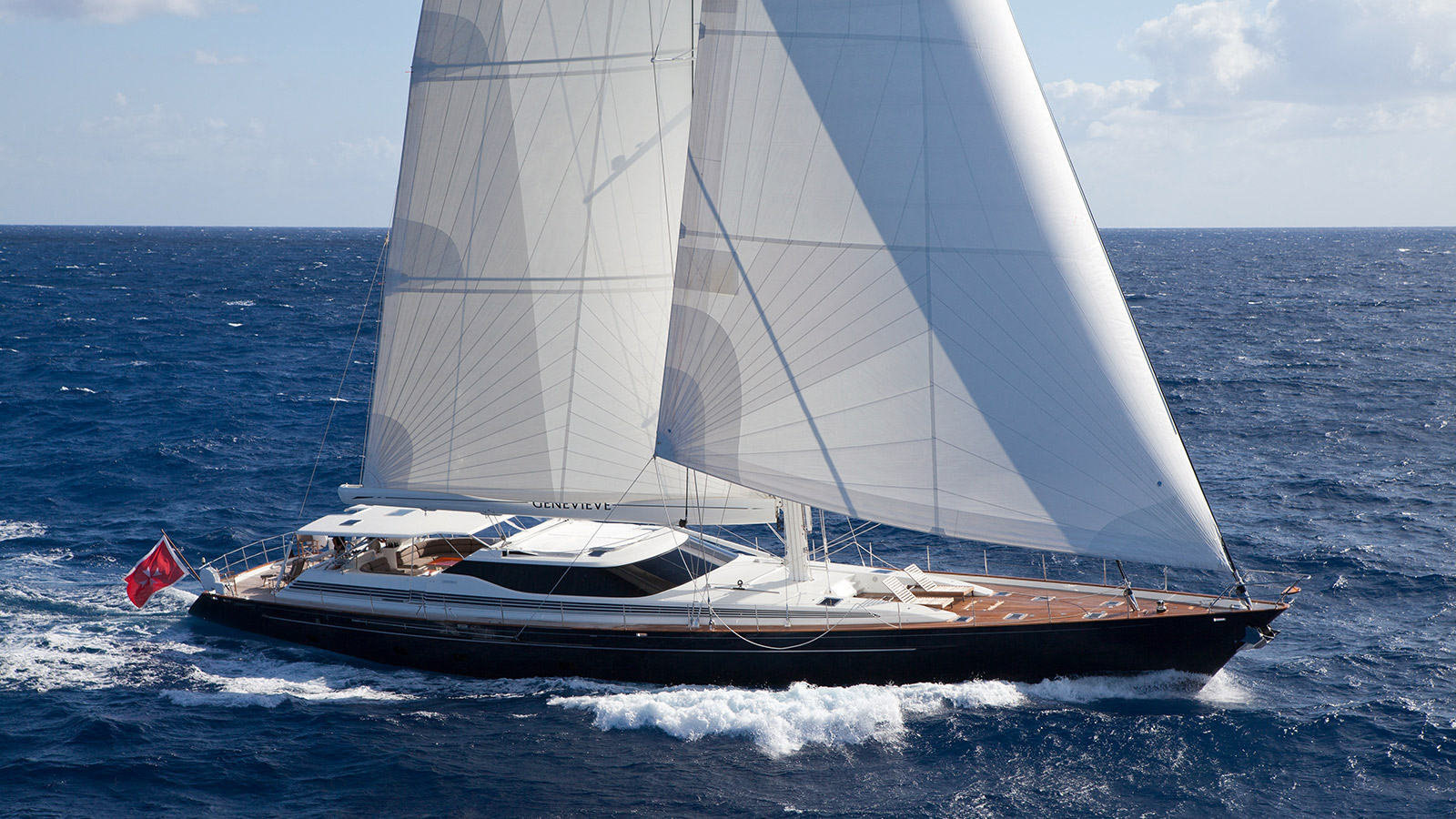 Sailing yacht Genevieve cutting through ocean waves under full sail with classic design and teak decks.