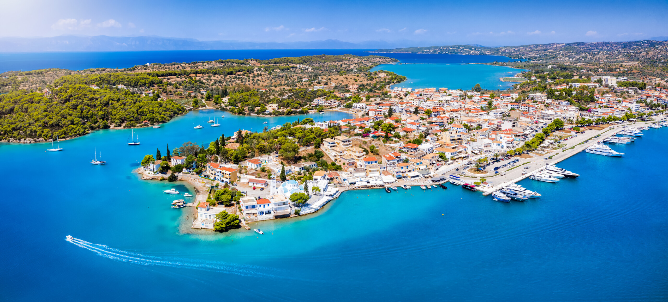 Aerial view of Porto Heli&rsquo;s marina and coastline with yachts, turquoise bays, and surrounding greenery.
