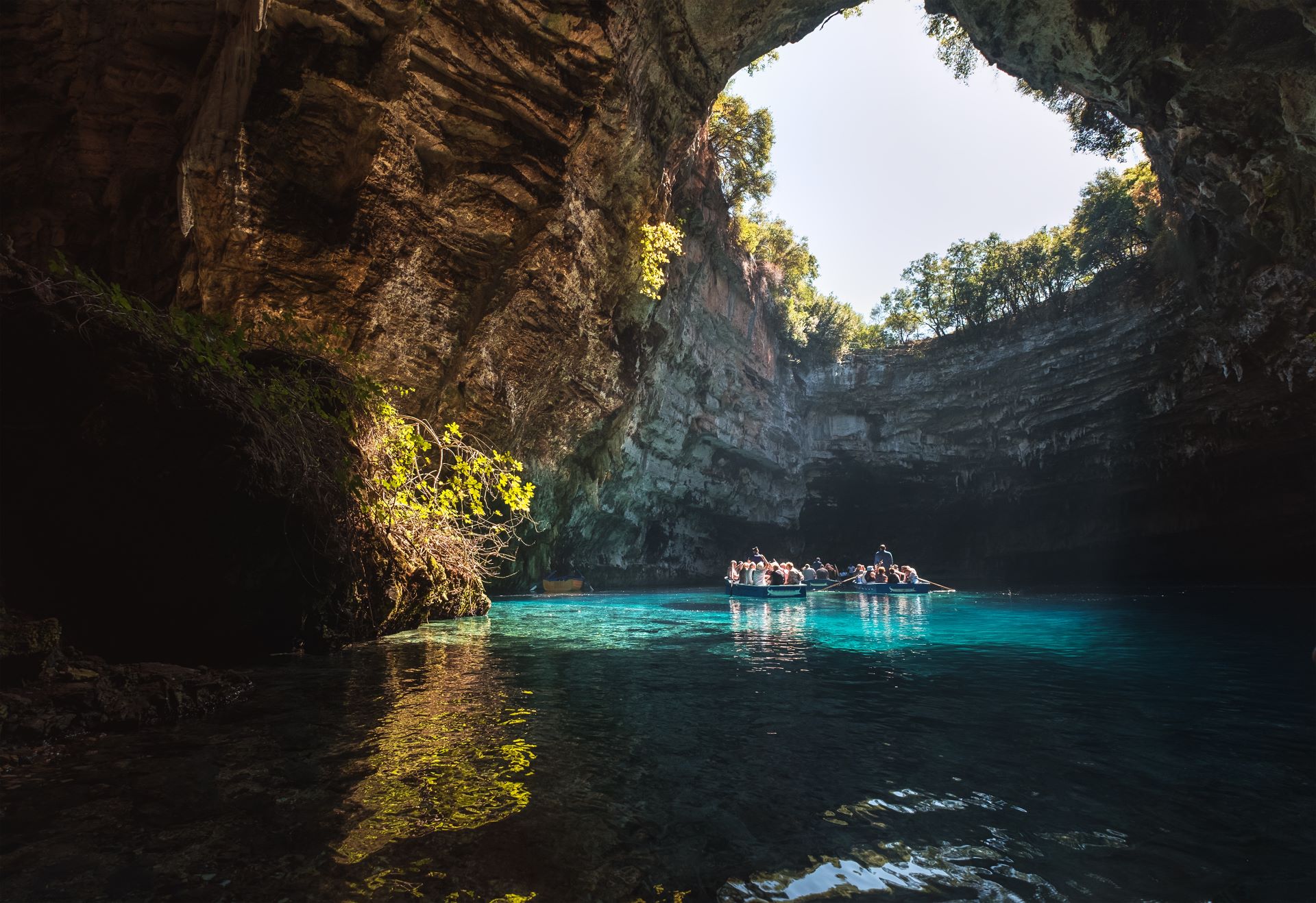 Tourists in rowboats exploring the turquoise waters of Melissani Cave Lake inside a collapsed limestone cave in Kefalonia, Greece.
