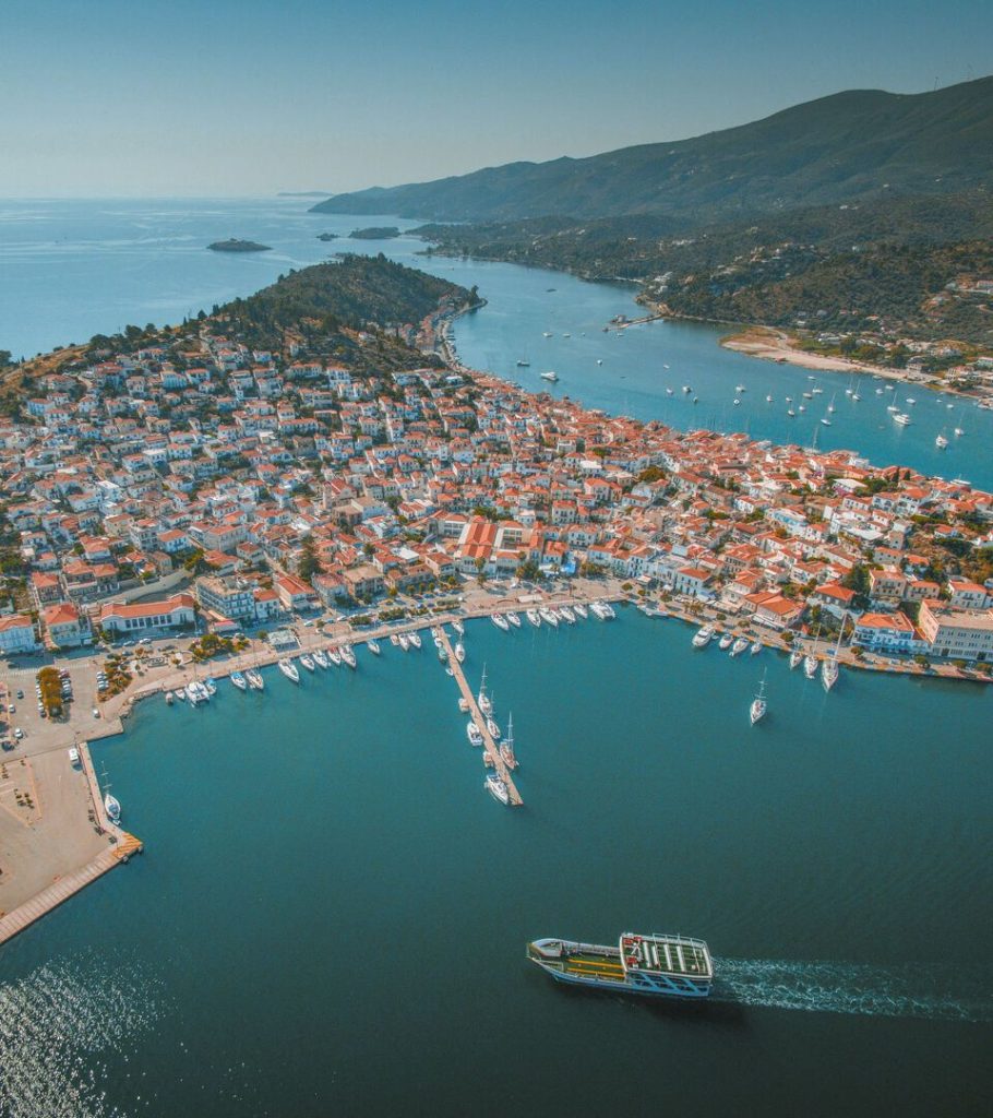 Aerial view of Poros Island, Greece, showing the harbor, red-roofed houses, and surrounding coastline.
