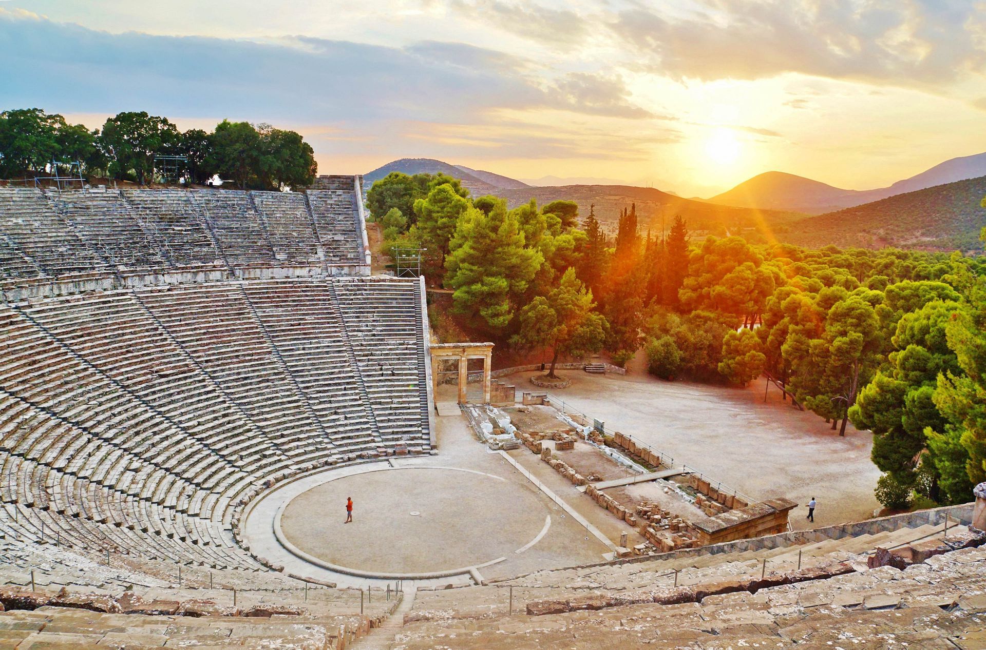 Ancient amphitheater of Epidaurus at sunset, surrounded by pine-covered hills in the Peloponnese.
