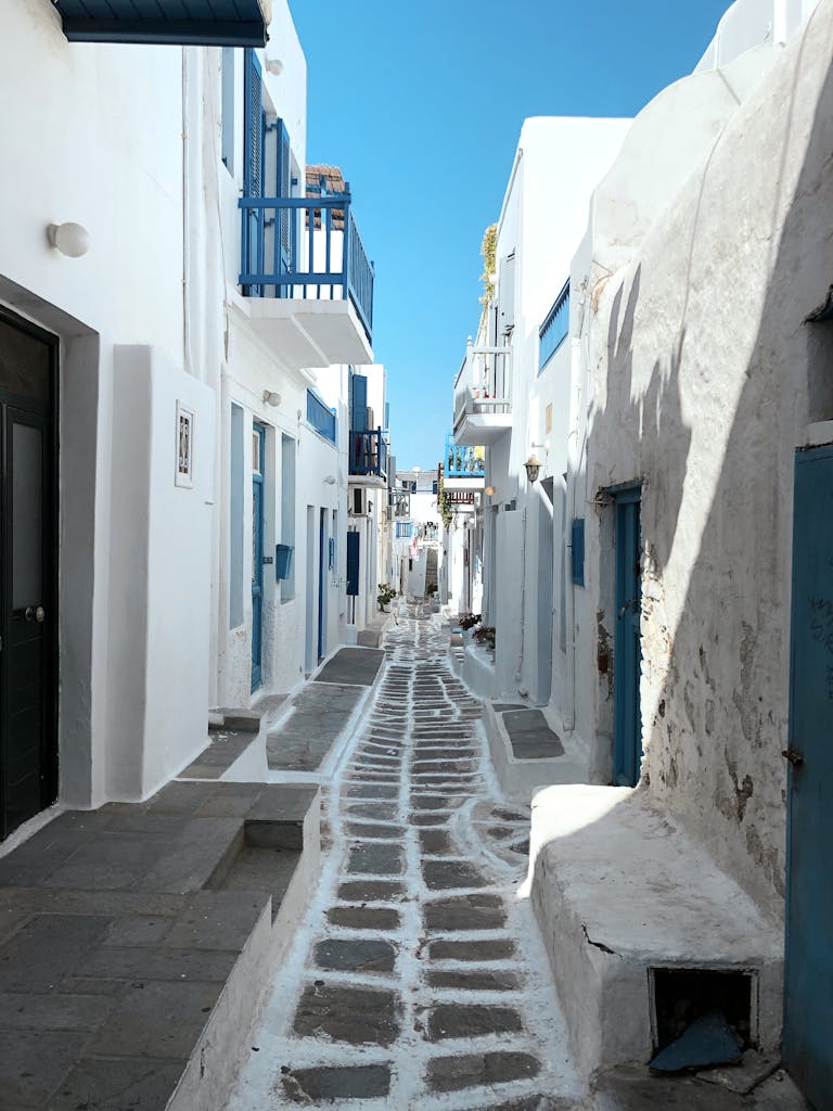 Explore the charming narrow streets of Mykonos, Greece, with iconic whitewashed buildings and blue accents.