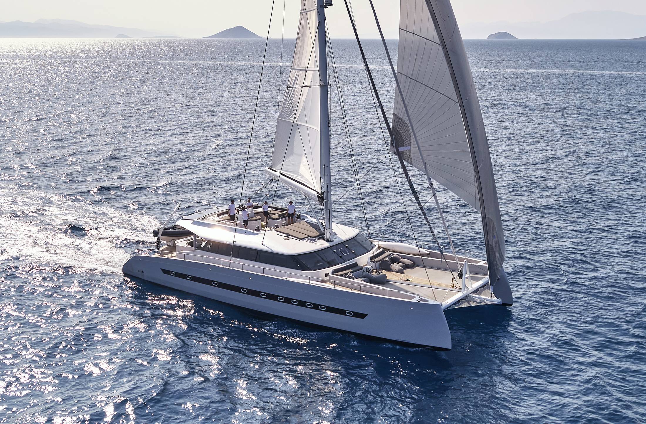 Luxury sailing catamaran cruising under sail in calm blue waters with crew on deck.