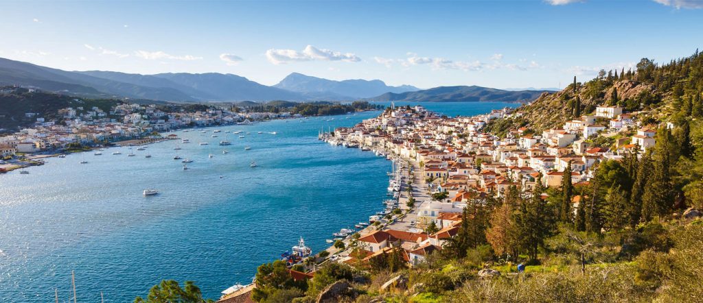 Scenic panoramic view of Poros island, Greece, with traditional white houses, lush hills, and yachts anchored in the bay.