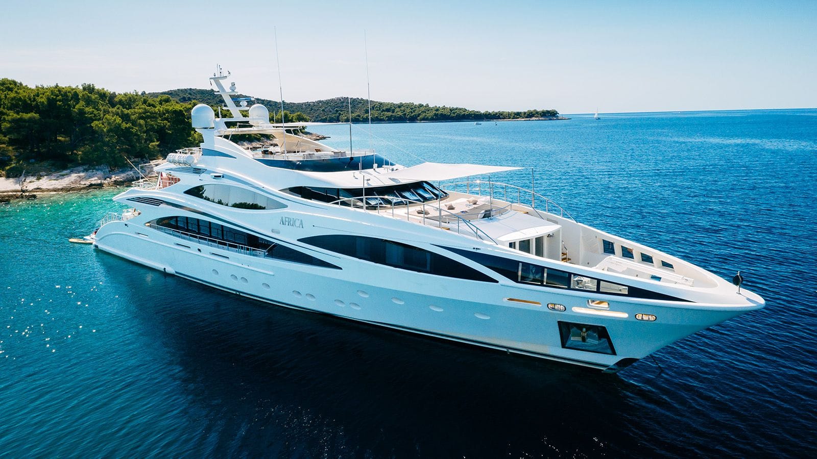 Luxury yacht AFRICA I anchored in a secluded turquoise bay with a forested coastline in the background.
