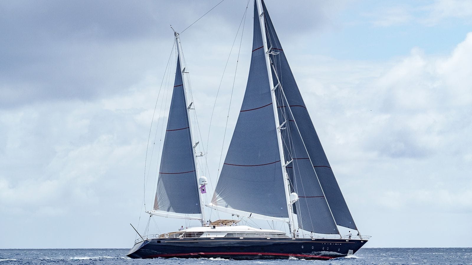 ALMYRA II sailing yacht cruising under full sail in open waters with a cloudy sky backdrop.
