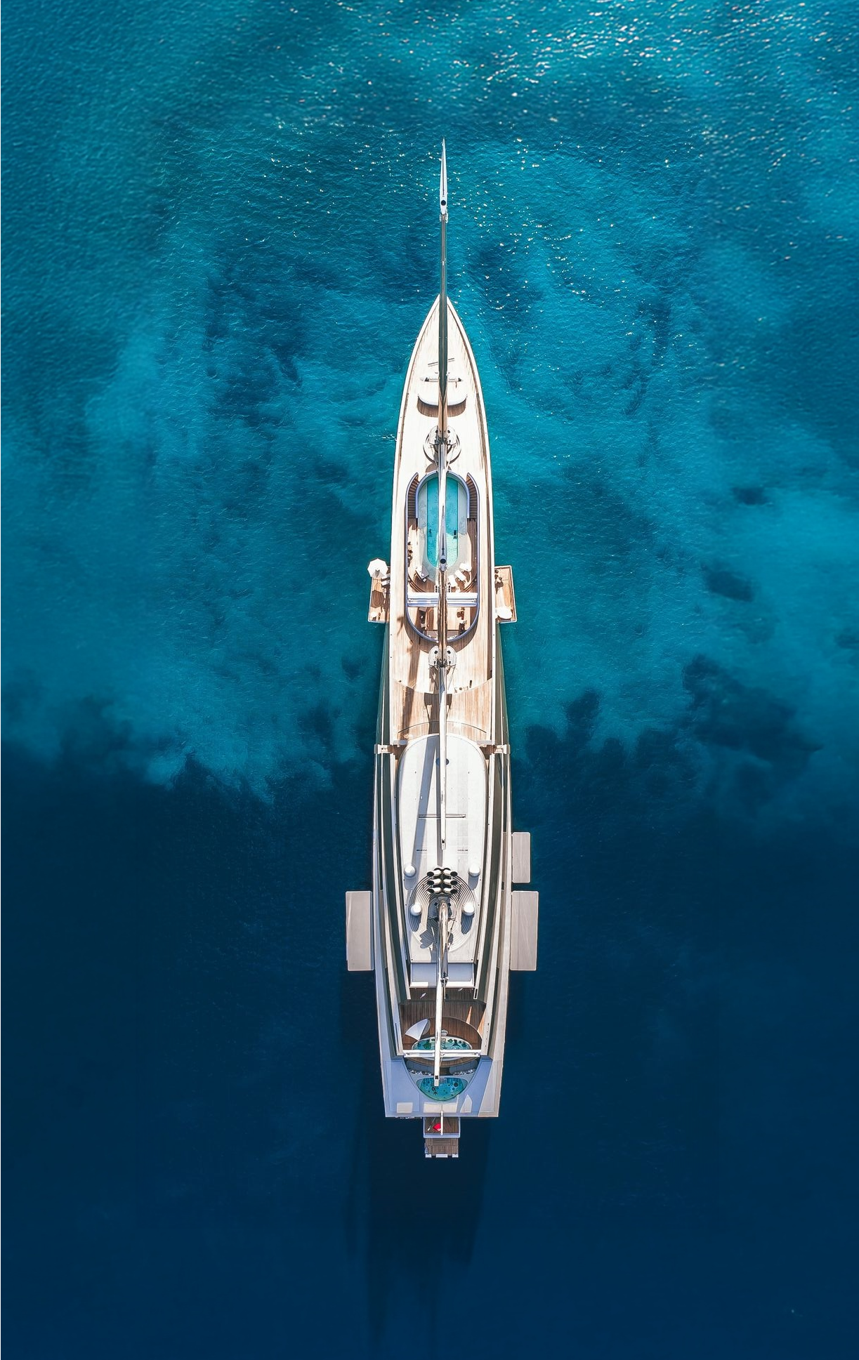 Top-down view of the futuristic sailing yacht SY A floating on vibrant turquoise water.